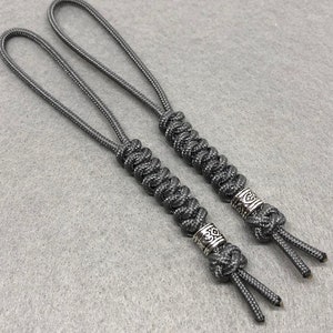 May include: Two gray paracord keychains with silver metal beads. The beads have a decorative design.