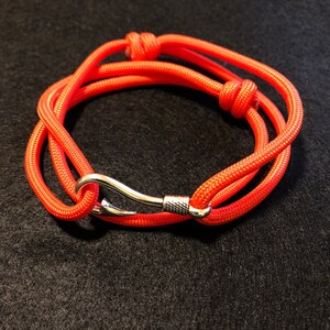 May include: A bright orange paracord bracelet with a silver hook clasp.