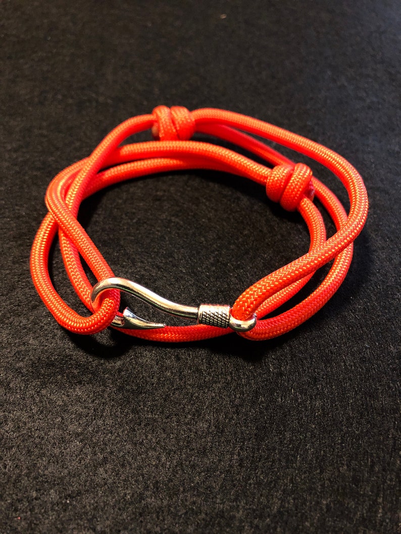 May include: A bright orange paracord bracelet with a silver hook clasp.