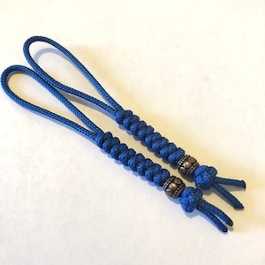 May include: Two blue cord keychains with a decorative metal bead on each. The beads are a dark copper color and have a textured design.