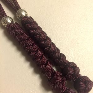 May include: Two maroon paracord lanyards with silver metal beads at the ends. The lanyards are braided and knotted.