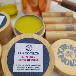 Pode incluir: Uma imagem de produtos naturais para cuidados com a pele. Um frasco de bálsamo de cera de abelha amarelo com o rótulo "CHAMOMILON LAVENDER BEESWAX BALM". Outros itens incluem protetores labiais, uma panela de cobre e um béquer com líquido amarelo.