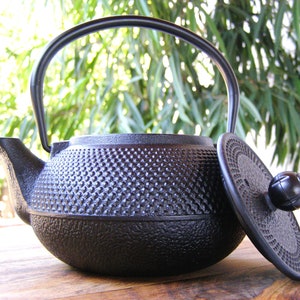 May include: Black cast iron teapot with a textured surface and a matching lid. The teapot has a round body and a curved spout.