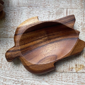 May include: A wooden turtle-shaped dish with a smooth, polished surface. The dish is made of a dark brown wood with visible grain patterns. The turtle design includes a central bowl area and four flipper-like extensions.