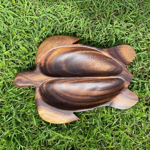 Peut inclure: Un plat de service en bois en forme de tortue avec trois compartiments séparés. Le plat est en bois brun foncé avec un motif de grain naturel.
