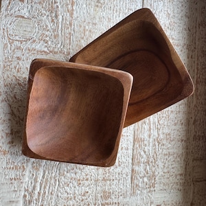 May include: Two square wooden bowls made of dark brown wood. The bowls are nested together, with the smaller bowl on top.