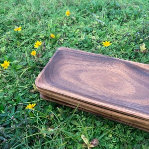 May include: A set of four rectangular wooden serving trays stacked on top of each other. The trays are made of dark brown wood and have a smooth, polished finish.