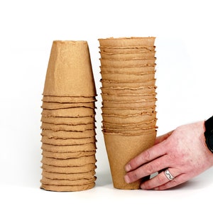 May include: A stack of brown biodegradable pots for planting, made from recycled paper pulp. The pots are stacked on a white surface.