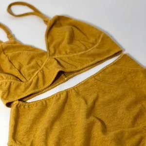 May include: Mustard yellow lingerie set. The set includes a triangle-style bralette with adjustable straps and high-waisted bottoms. The fabric has a textured appearance and visible stitching.