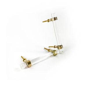 May include: Two clear acrylic cabinet knobs with gold metal accents. The knobs are in the shape of a cylinder with a rounded end.