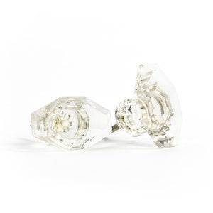 Puede incluir: Dos pomos de puerta de vidrio transparente con un diseño facetado. Los pomos tienen un vástago de metal plateado.