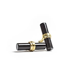 May include: A pair of black cufflinks with gold accents. The cufflinks are cylindrical in shape and have a smooth, polished finish.