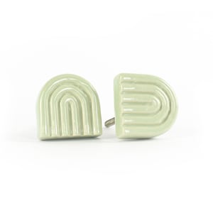 Op de afbeelding: Twee keramische kastknoppen in een lichtgroene kleur met een reliëf boogontwerp.