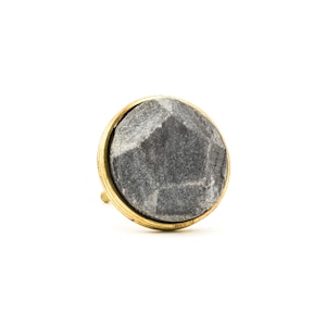May include: A round, grey stone knob with a gold metal rim. The knob has a textured, faceted surface.