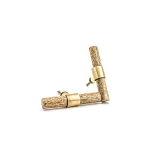 May include: Two wooden cabinet knobs with brass accents. The knobs are in the shape of a short, thick cylinder with a brass ring around the centre. The knobs are arranged in an L-shape.