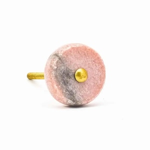 May include: A pink and grey marble cabinet knob with a gold metal accent.