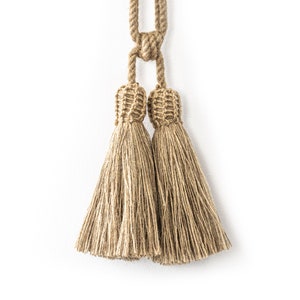 May include: Two brown tassel tiebacks made of natural fibre rope. The tassels are tied together with a knot at the top.