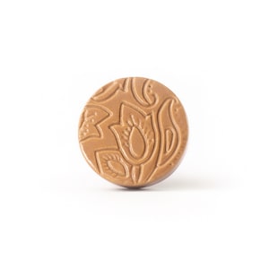 May include: A round, brown button with a floral design. The button has a raised, embossed pattern of flowers and leaves.