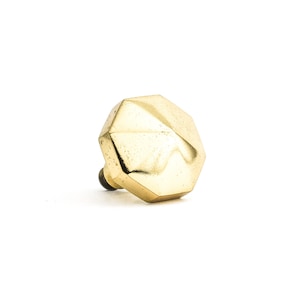 May include: A gold-coloured, faceted cabinet knob with a dark brown screw. The knob has a geometric, multi-sided design and a slightly distressed finish. Suitable for drawers and cabinets.