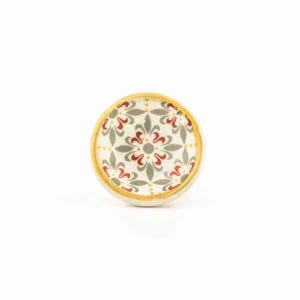 May include: A round ceramic knob with a yellow rim and a white background. The knob features a repeating pattern of red and grey stylised flowers.
