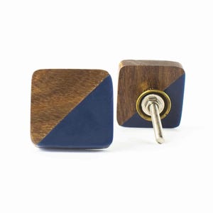 May include: Two square wooden cabinet knobs. Each knob is divided diagonally, with a dark blue section and a brown wood section. The knobs have a metal screw and a brass-coloured ring for attachment. The knobs are designed for furniture.