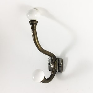 May include: Antique brass coat hook with two white ceramic knobs.