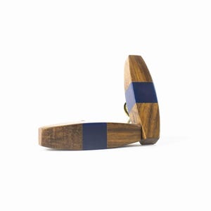 May include: Two wooden cabinet pulls with a dark blue accent. The pulls are made of a light brown wood with a dark blue band in the centre. The pulls are connected by a gold-coloured metal ring.
