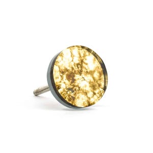 May include: A cabinet knob with a circular, gold-coloured face displaying a mottled pattern. It has a dark grey rim and a silver threaded post. This modern design is suitable for furniture, such as drawers or cabinets.