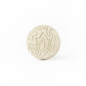 Peut inclure: Un bouton rond en céramique blanc cassé avec un motif floral en relief. Le motif présente une fleur centrale avec un motif de type paisley autour.
