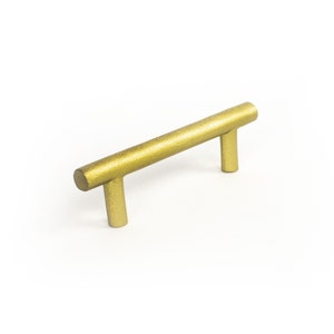 May include: A gold-coloured metal cabinet pull with a straight bar and two rounded ends. The pull is approximately 10 cm long.