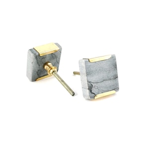 May include: Two square grey marble cabinet knobs with gold trim. Each knob has a screw for installation.