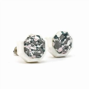 May include: A pair of white octagonal stud earrings with a grey, pink and green marbled design.