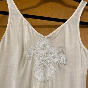 May include: White sleeveless slip with a delicate white lace and pearl embellishment on the front.