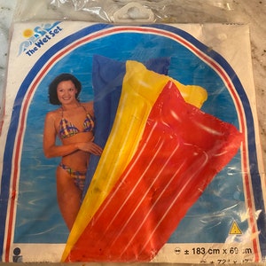 May include: A set of three inflatable pool floats in red, yellow, and blue. The floats are stacked on top of each other and have a striped pattern. The packaging includes the text "The Wet Set" and a warning symbol. The dimensions of the floats are approximately 183 cm x 69 cm.