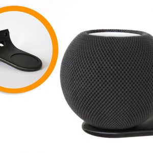 May include: Black wall mount for a round, black speaker with a mesh pattern. The mount has a curved design and a small platform for the speaker to rest on.