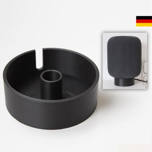 Könnte beinhalten: Ein schwarzer 3D-gedruckter Ständer für einen intelligenten Lautsprecher. Der Ständer hat eine runde Basis und ein zentrales Loch für das Kabel des Lautsprechers.