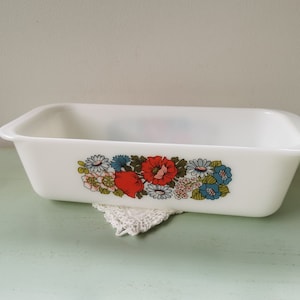 Pode incluir: Forma de pão de cerâmica branca com um design floral com flores vermelhas, azuis e verdes. A forma está sobre uma renda branca.