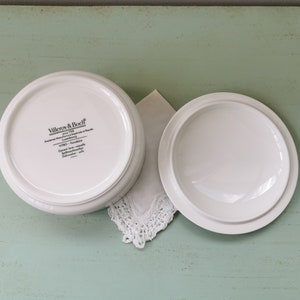 May include: White ceramic lidded dish with the text "Villeroy & Boch" and "Anmut" on the bottom. The dish is on a light green surface.