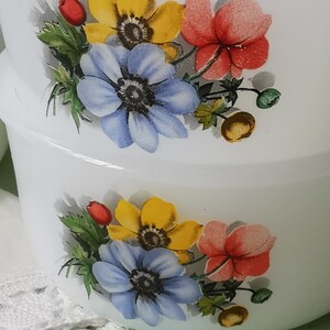 May include: Two white ceramic bowls with a floral design. The design features yellow, blue, and red flowers with green leaves. The bowls are stacked on top of each other.