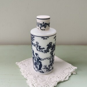 May include: A white porcelain bottle with a blue and white floral design. The bottle has a round shape and a small opening at the top. The design features a scene with people and trees.