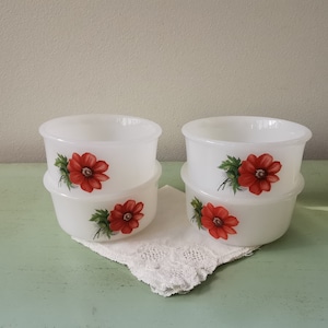 Op de afbeelding: Set van vier witte keramische kommen met rode bloemenmotieven. Elke kom heeft een rode bloem met groene bladeren op een witte achtergrond.