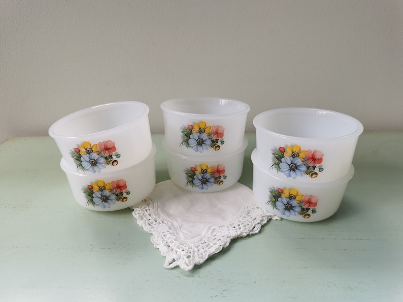 May include: Six white ceramic bowls with floral designs. The bowls are stacked in pairs and feature a blue, yellow, and pink floral pattern.