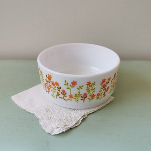 Peut inclure: Bol en céramique blanche avec un motif floral dans les tons orange, rose et vert. Le bol est posé sur une dentelle blanche.