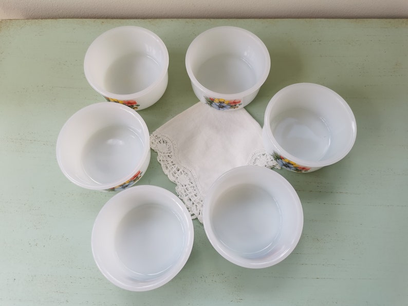 May include: Set of six white ramekins with floral designs. The ramekins are made of glass and have a smooth, white finish. They are perfect for serving desserts, dips, or other small dishes.