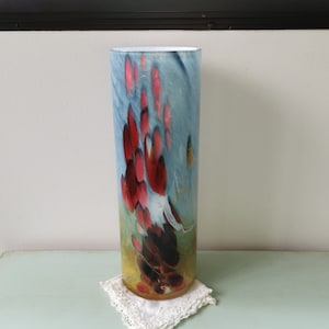 May include: A tall, cylindrical glass vase with a blue, white, and yellow background. The vase has a red and brown abstract design.