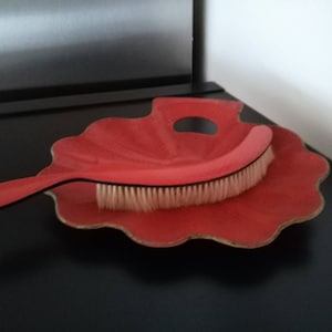 May include: A red, shell-shaped dustpan with a matching red and black brush. The brush has white bristles.