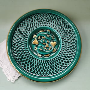 Peut inclure: Une assiette en céramique verte avec un bord doré et un motif en relief de trois poissons dorés au centre. L'assiette présente un motif décoratif tissé autour du bord.