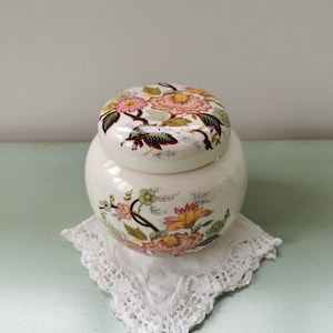 Peut inclure: Un pot en céramique blanche avec un motif floral. Le couvercle et le pot ont un motif floral assorti avec des fleurs roses, jaunes et vertes.