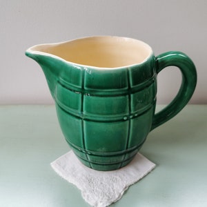 May include: A green ceramic pitcher with a white interior and a checkered pattern. The pitcher has a rounded body and a handle.