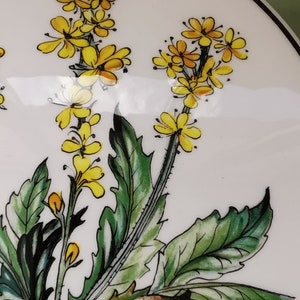 May include: A white ceramic plate with a hand-painted design of yellow flowers and green leaves.